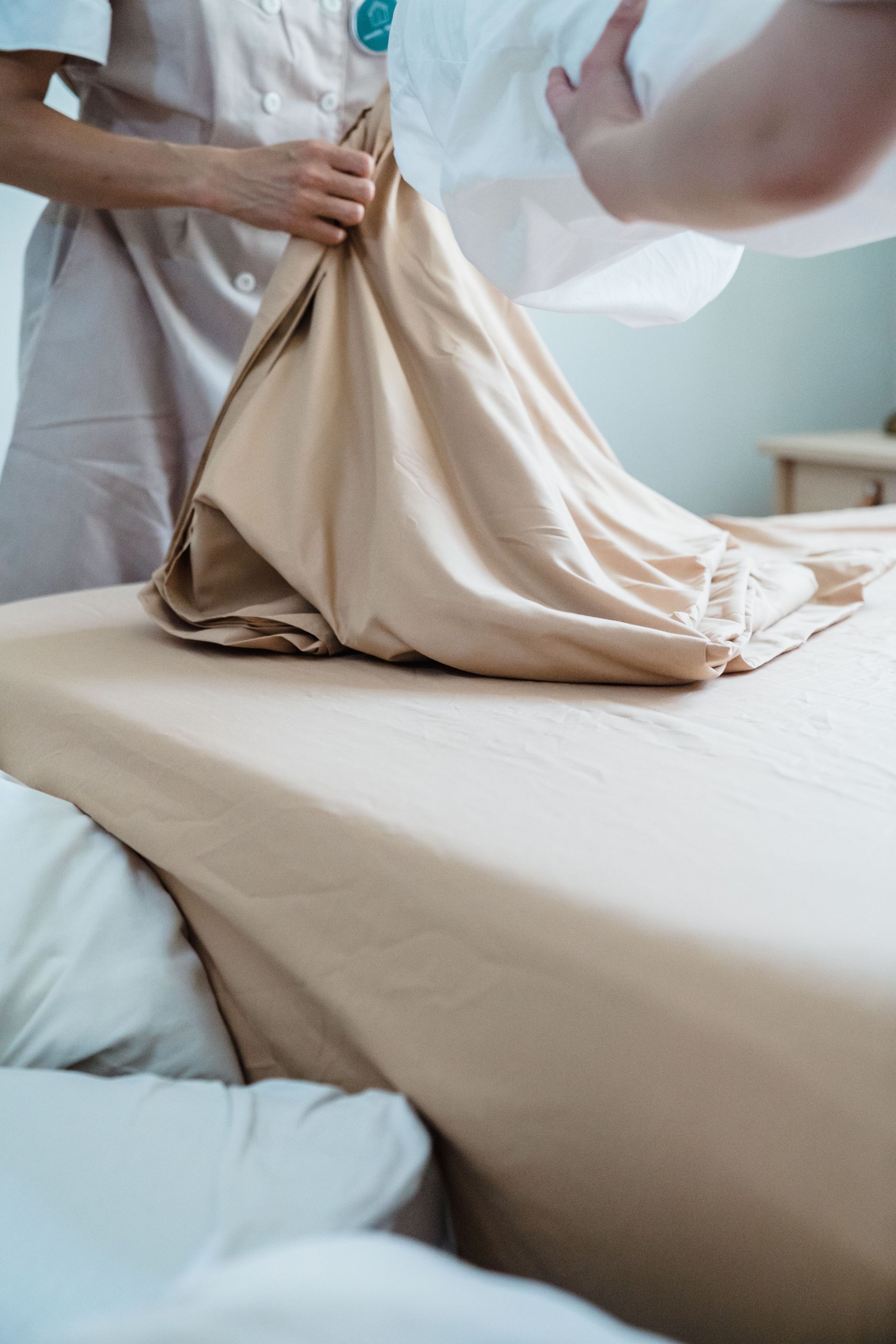 Housekeeper smoothing out bed linens, ensuring neatness in a hotel room setup.